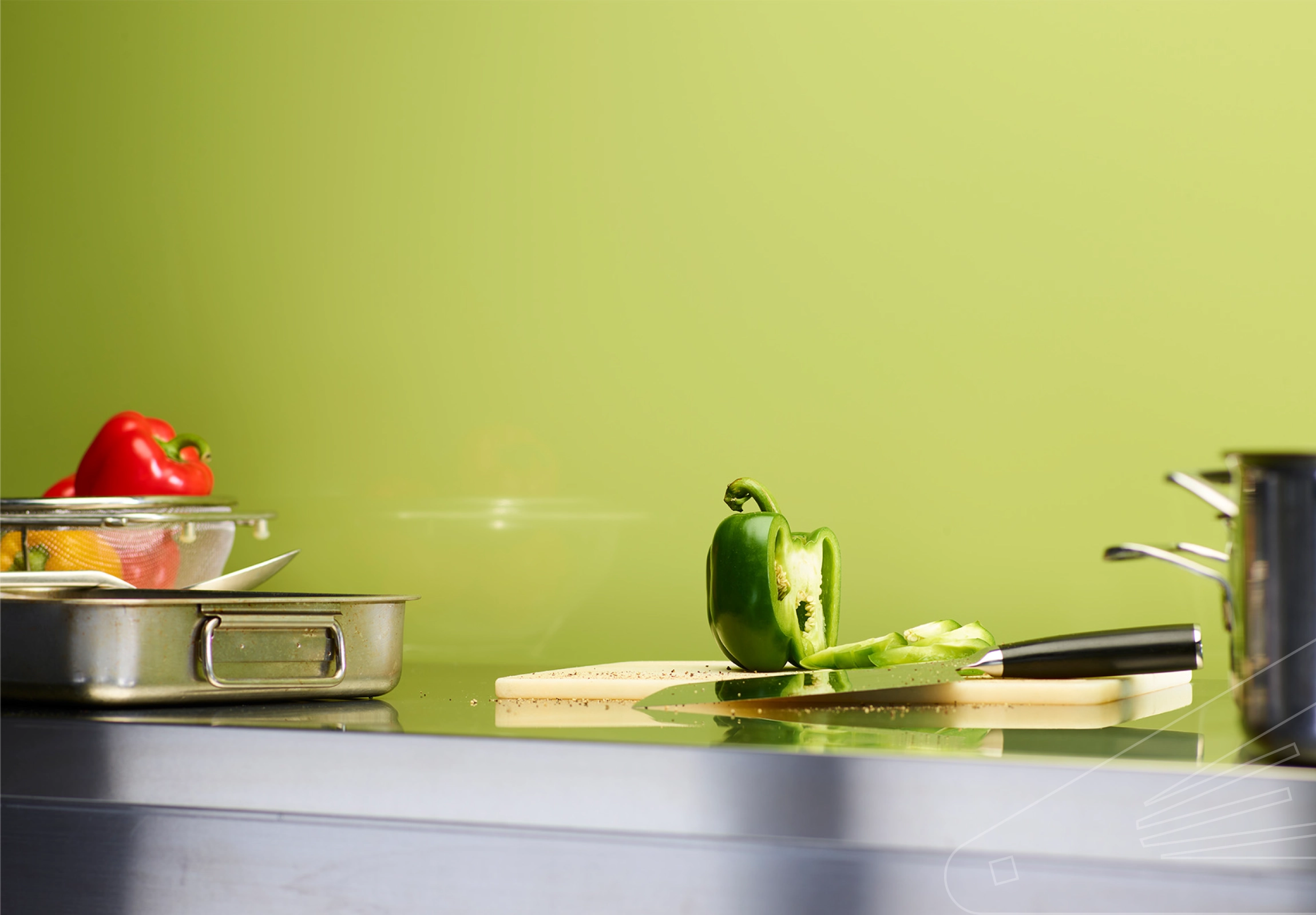 Cladding installed above a stainless steel kitchen worktop. The surface is holding a chopping board, pans, utensils, and various colourful peppers.
