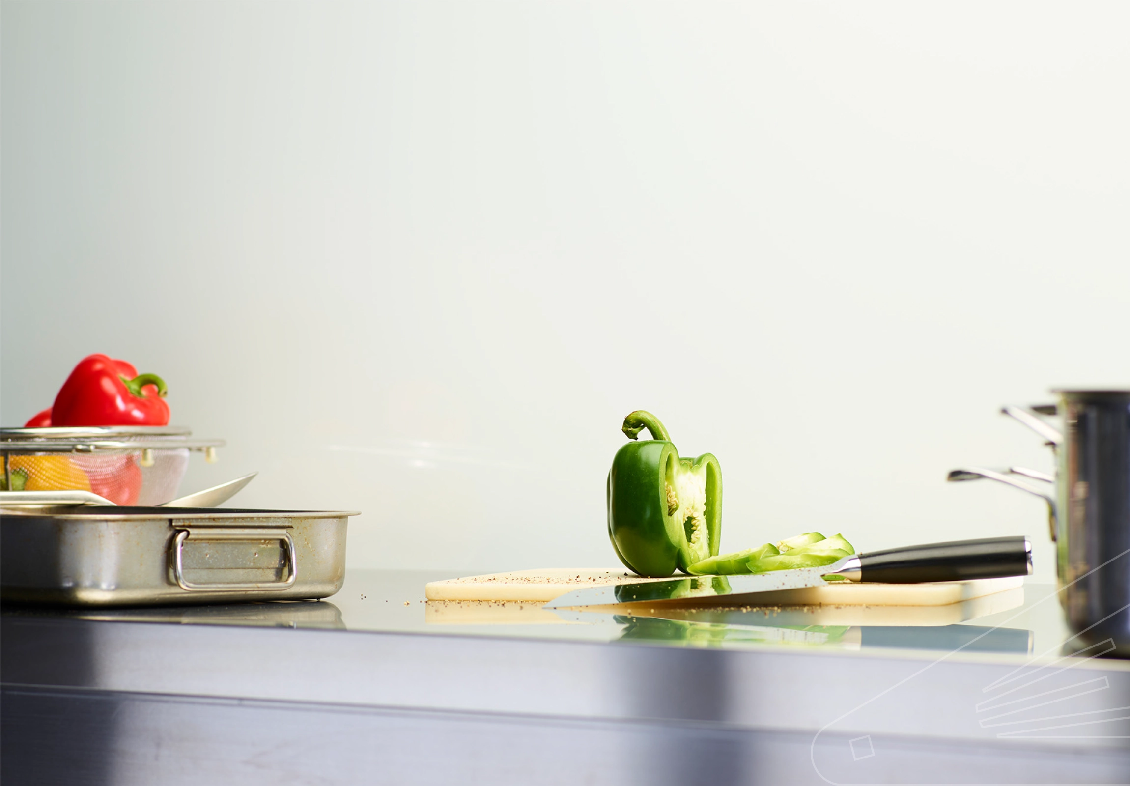 White Gloss Cladding installed above a stainless steel kitchen worktop. The surface has a chopping board, pans, utensils, and various colourful peppers.
