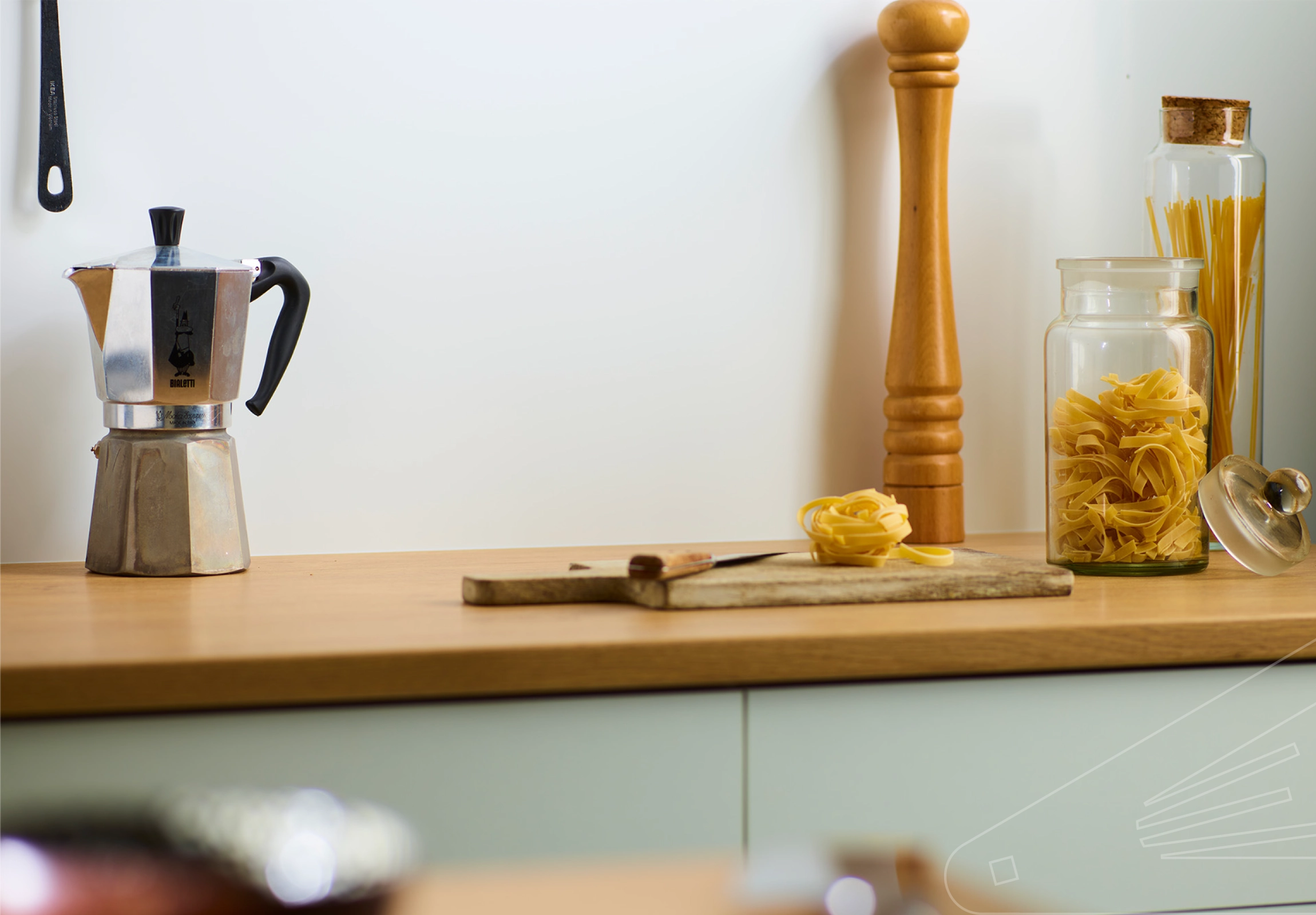 White Satin Cladding installed above a wooden kitchen worktop. The surface is holding a chopping board, glass storage jars and a coffee percolator.