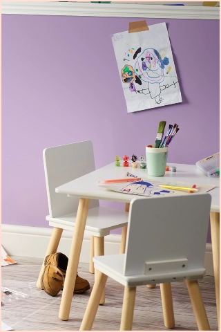 Children’s playroom with a small table and chairs, drawing supplies, children’s artwork on a Lavender Satin cladding wall and toys on the floor.