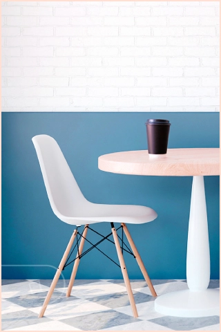Minimal café-style interior with a white chair and round table holding a takeaway coffee cup against a bottom half clad wall with Aqua Satin plastic cladding and white brick wall above.