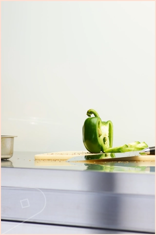 A Linen clad wall behind kitchen countertop with a sliced green bell pepper on a cutting board, seeds scattered nearby and a pot in the background.
